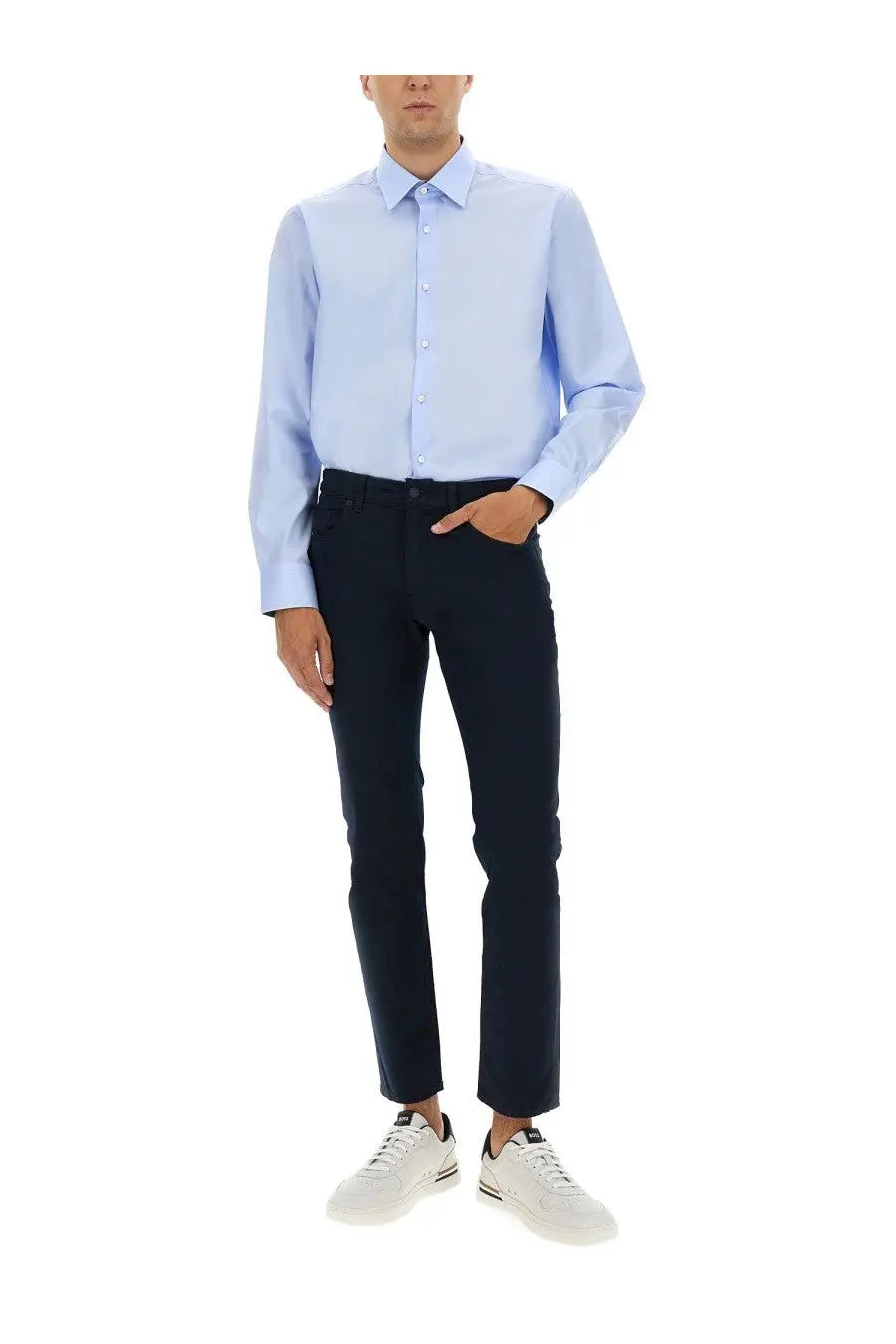 A man wearing a boss men’s poplin shirt blue in light blue with dark navy slim-fit trousers and white sneakers