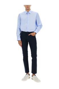 A man wearing a boss men’s poplin shirt blue in light blue with dark navy slim-fit trousers and white sneakers