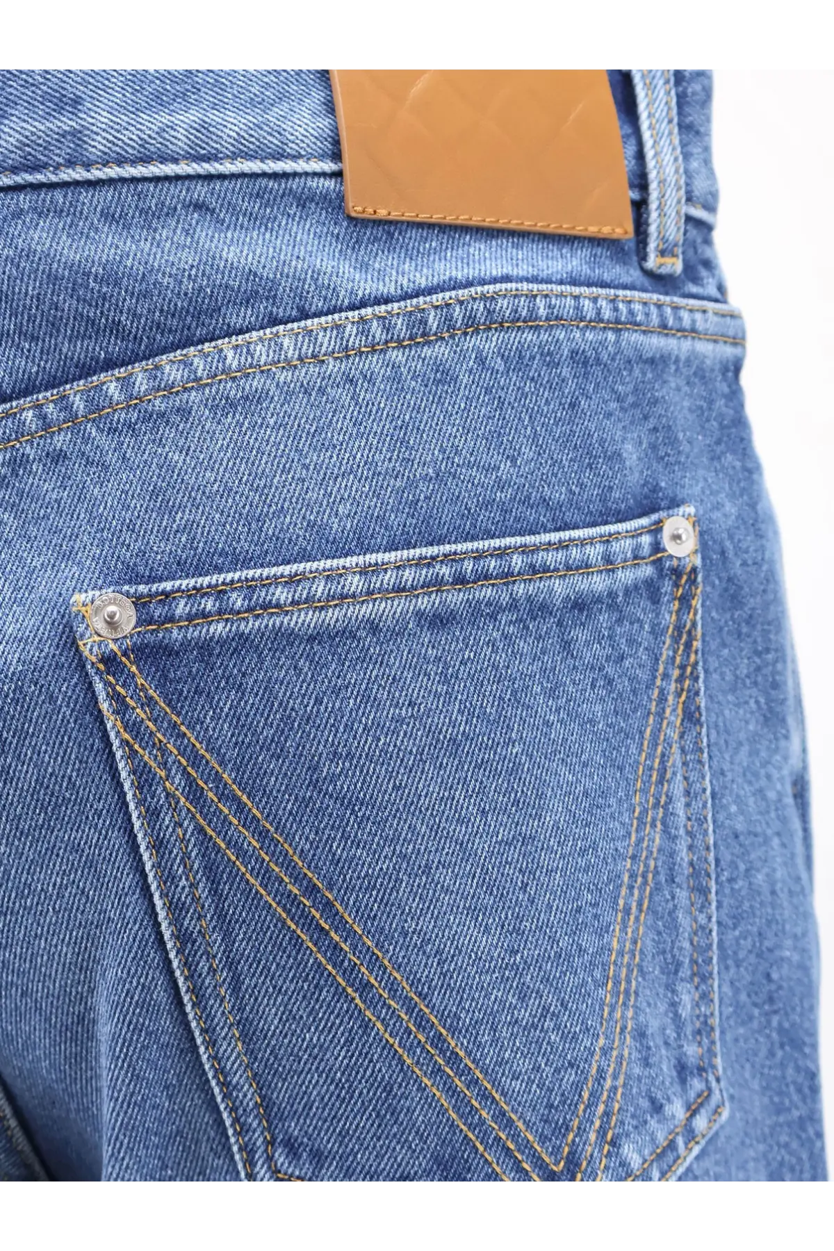 Back side of Bottega Veneta men’s regular cotton jeans in medium-wash blue denim with brown leather patch and silver rivets