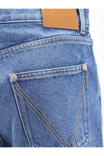 Back side of Bottega Veneta men’s regular cotton jeans in medium-wash blue denim with brown leather patch and silver rivets