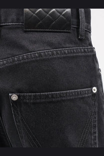 Back view of bottega veneta women’s black denim trousers with quilted leather waistband patch and silver rivets