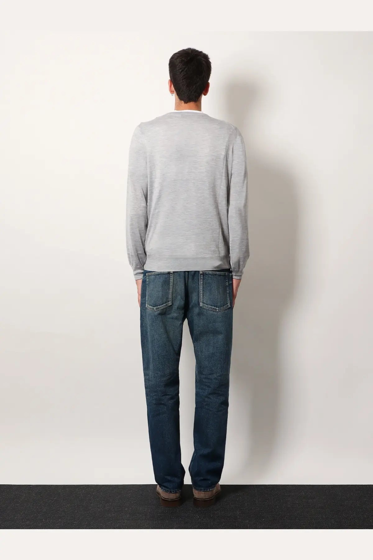 A man wearing a brunello cucinelli men’s grey cashmere and silk knit sweater with long sleeves and dark blue jeans