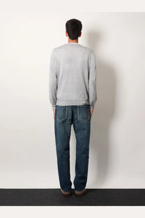 A man wearing a brunello cucinelli men’s grey cashmere and silk knit sweater with long sleeves and dark blue jeans