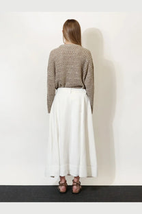 A woman wears a beige knitted sweater over white high-waisted wide-leg trousers in brunello cucinelli viscose and linen skirt white
