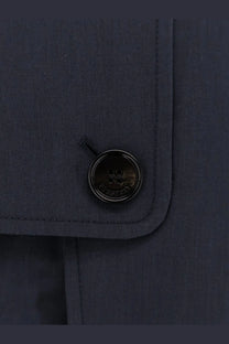 Black circular button with embossed Burberry logo on dark navy cotton blend fabric of Burberry men’s Highbury trench