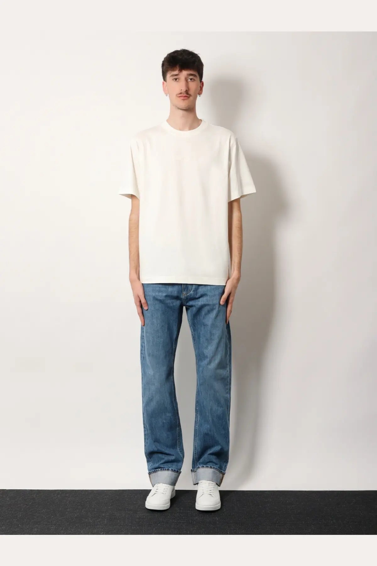A man wearing a Burberry men’s Ryan organic cotton white short-sleeved crew neck t-shirt with blue jeans and white sneakers