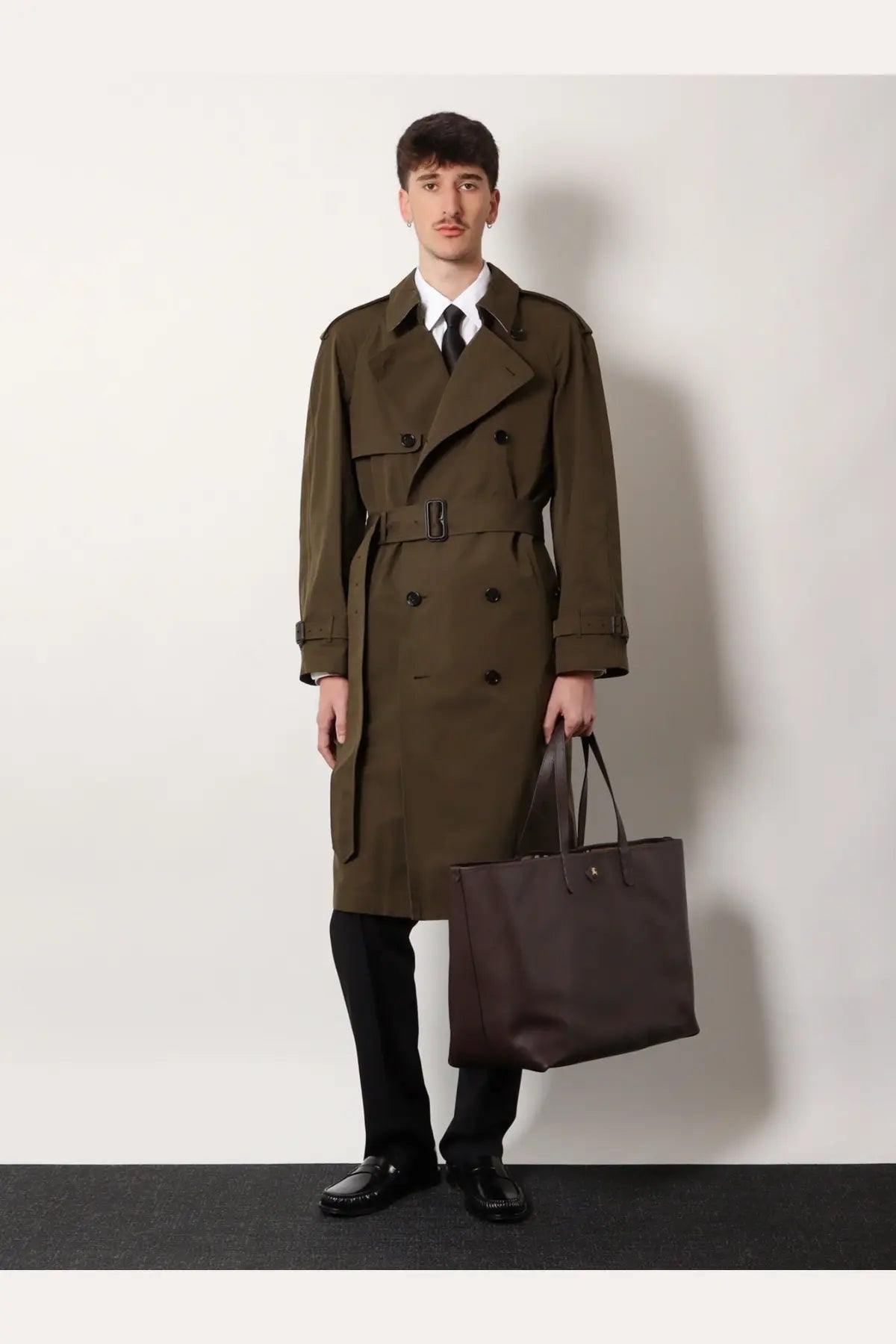 Olive green double-breasted trench coat with black belt and dark brown leather handles paired with burberry men’s white organic cotton shirt