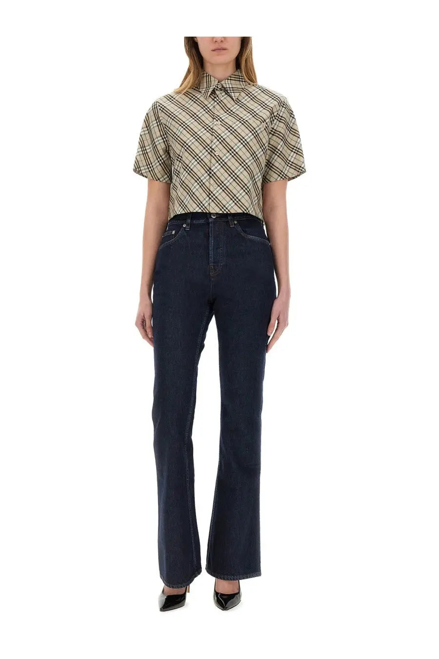 A woman wears a Burberry women’s cropped short-sleeved beige and black plaid button-up shirt with dark blue flared jeans
