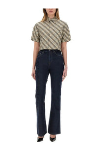 A woman wears a Burberry women’s cropped short-sleeved beige and black plaid button-up shirt with dark blue flared jeans