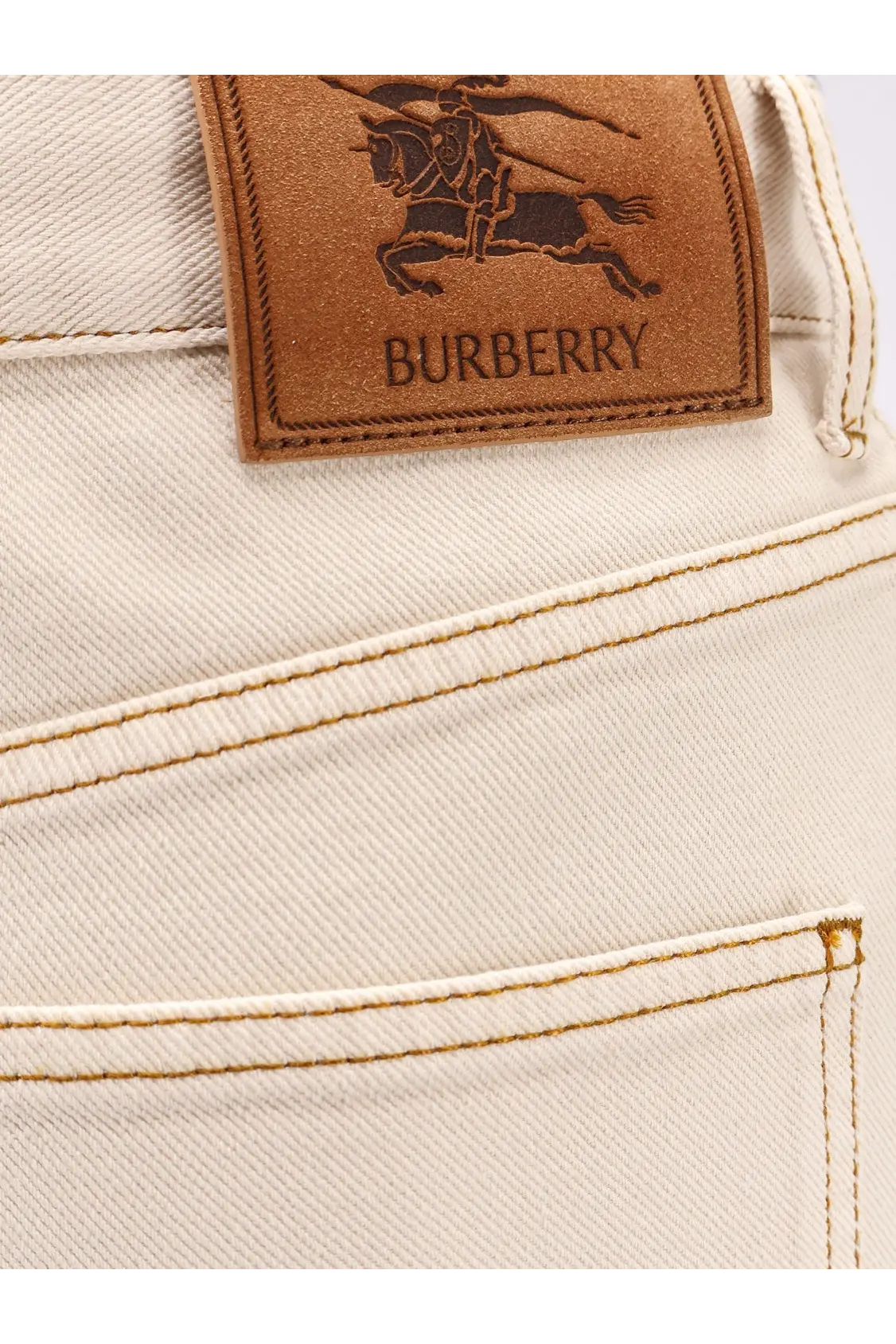 Cream-colored burberry women’s denim trousers with a brown leather patch featuring the burberry knight logo on back