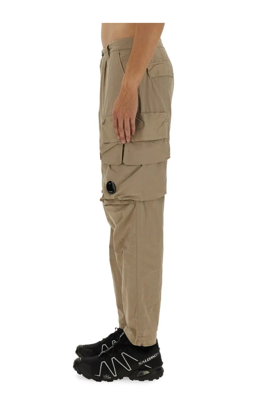 C.P. Company men’s beige cargo pants featuring multiple pockets and a black circular button detail on the thigh