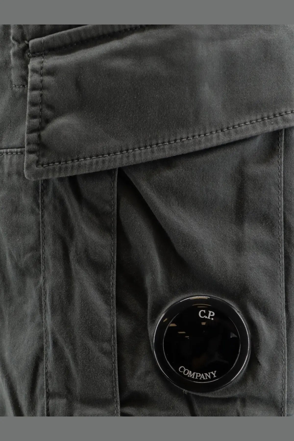 Dark gray cotton canvas jacket with circular black cp company logo patch and men’s cargo bermuda shorts in grey