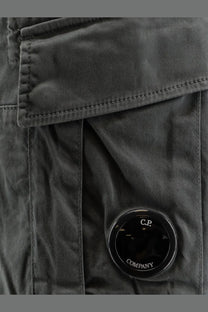 Dark gray cotton canvas jacket with circular black cp company logo patch and men’s cargo bermuda shorts in grey