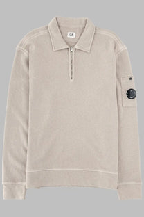 Beige textured knit polo shirt with half-zip front and black circular logo patch on the sleeve by C.P. Company
