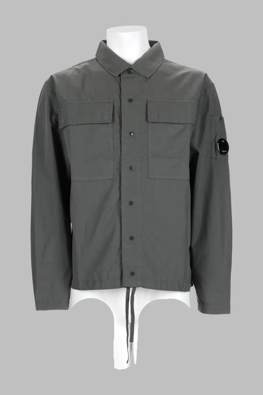 Dark gray long-sleeved c.p. company men’s overshirt with button-up front, two chest pockets, and black sleeve logo patch