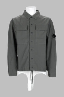 Dark gray long-sleeved c.p. company men’s overshirt with button-up front, two chest pockets, and black sleeve logo patch