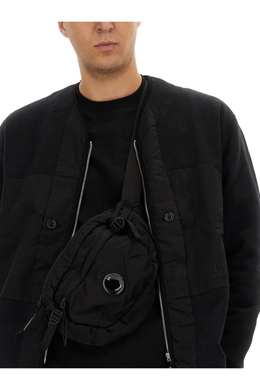 Black circular crossbody bag with prominent lens-style zipper pull and multiple zippers for stylish carrying