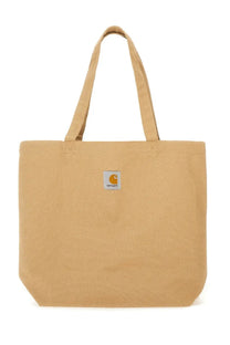 Tan canvas tote bag with small white logo patch on front by Carhartt Wip for men in beige color