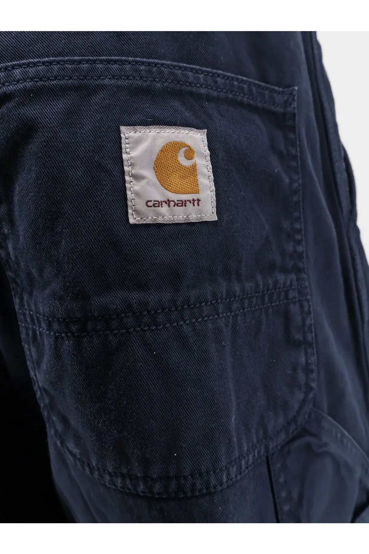 Dark blue carhartt wip men’s loose fit denim jeans with classic patch orange logo and white stitching on back pockets