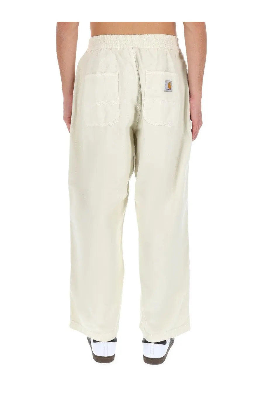 Back view of cream-colored carhartt wip men’s relaxed-fit cargo pants with elastic waistband and logo patch