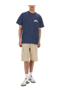 Navy blue short-sleeved t-shirt with white cursive logo on chest shown with carhartt wip men’s short cargo beige pants