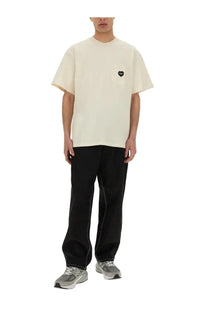 Cream-colored oversized t-shirt with a small black heart patch on the left chest pocket styled with carhartt wip men’s black single knee pant