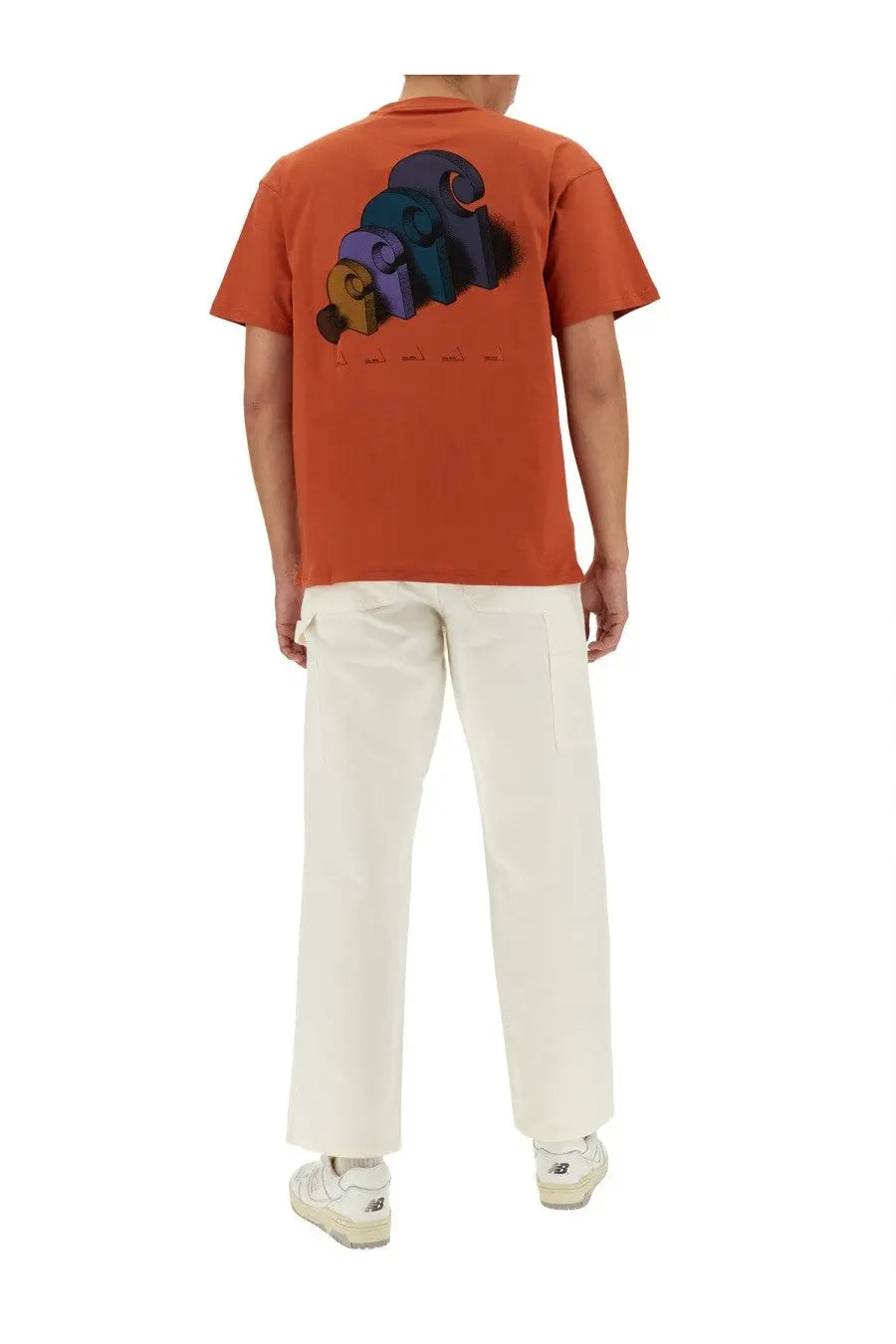 Back view of orange short-sleeved t-shirt with colorful 3d graphic print paired with carhartt wip men’s white single knee pants