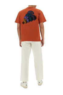 Back view of orange short-sleeved t-shirt with colorful 3d graphic print paired with carhartt wip men’s white single knee pants