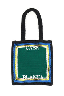 Black crocheted tote bag with green center panel bordered by blue and yellow featuring white casa blanca embroidery
