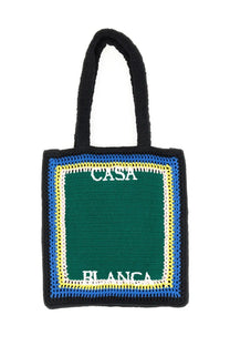 Black crocheted unisex tote bag with green center panel bordered by blue and yellow stripes and white casa blanca lettering
