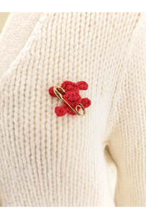 A red crocheted teddy bear pin with a gold safety pin clasp displayed with a celine women’s white silk and cashmere cardigan