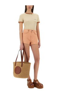 Beige woven tote bag with brown leather handles and circular leather patch paired with chloé women’s blue cotton shorts