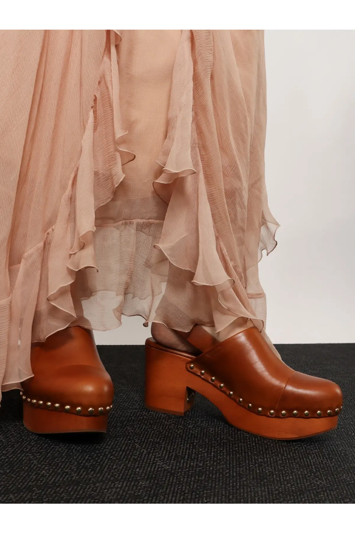 Brown leather clog shoes with a chunky wooden heel and metallic studs along the sole.