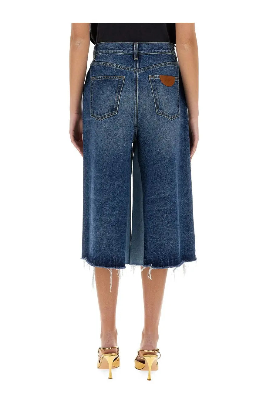 Back side of chloé women’s blue denim culottes with frayed hem and brown leather patch on the back pocket