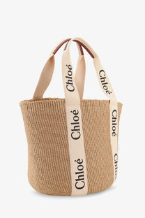 Beige woven raffia tote bag with cream straps and black chloé branding featured in chloé women’s woody collection