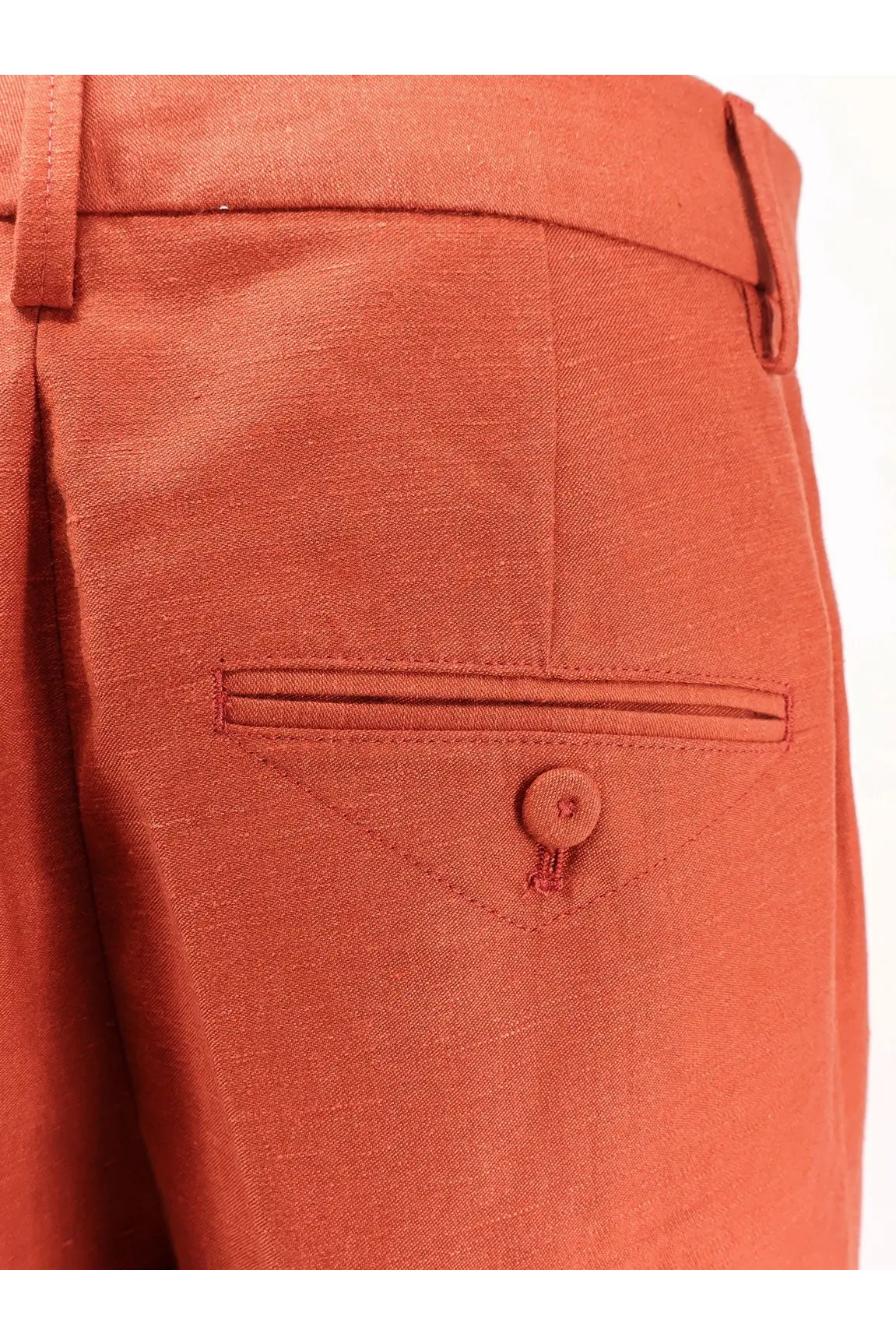 A pair of closed women’s jurdy cotton and linen rust-colored trousers with textured fabric and a buttoned flap pocket
