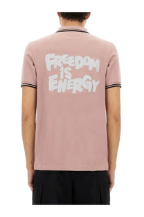 Comme des garcons shirt men’s dusty rose polo with black trim and white graffiti style freedom is energy graphic on back