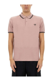A soft pink fred perry polo shirt with black trim and an embroidered logo on the chest from comme des garcons shirt