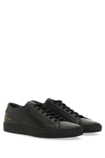 Common Projects men’s low-top black leather sneakers with minimalist design and subtle gold branding on the heel back side