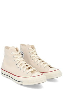 Cream-colored canvas high-top Converse unisex Chuck sneakers with red and black rubber soles and classic logo on the side