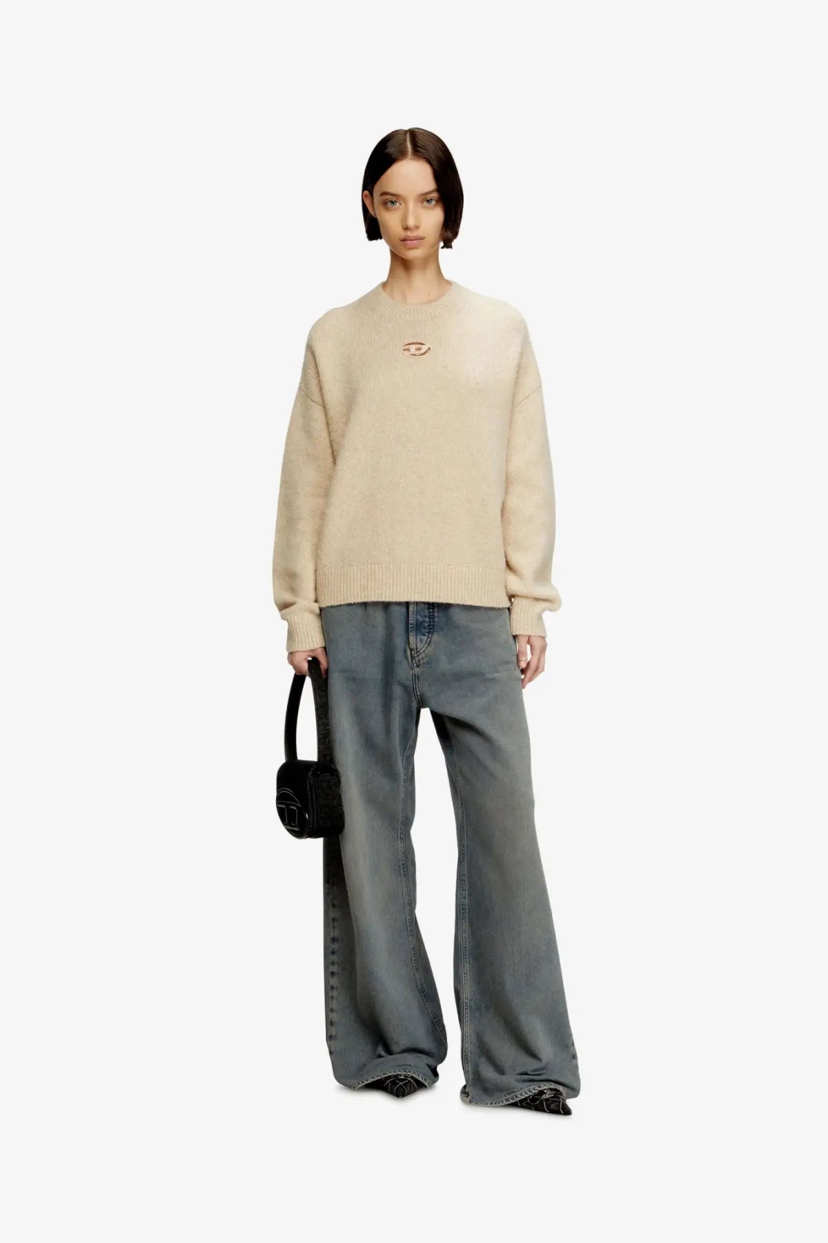 Beige oversized knit sweater with a small embroidered eye logo on the chest complementing diesel women’s black denim shoulder bag