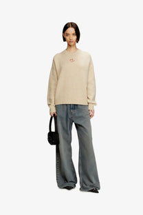 Beige oversized knit sweater with a small embroidered eye logo on the chest complementing diesel women’s black denim shoulder bag