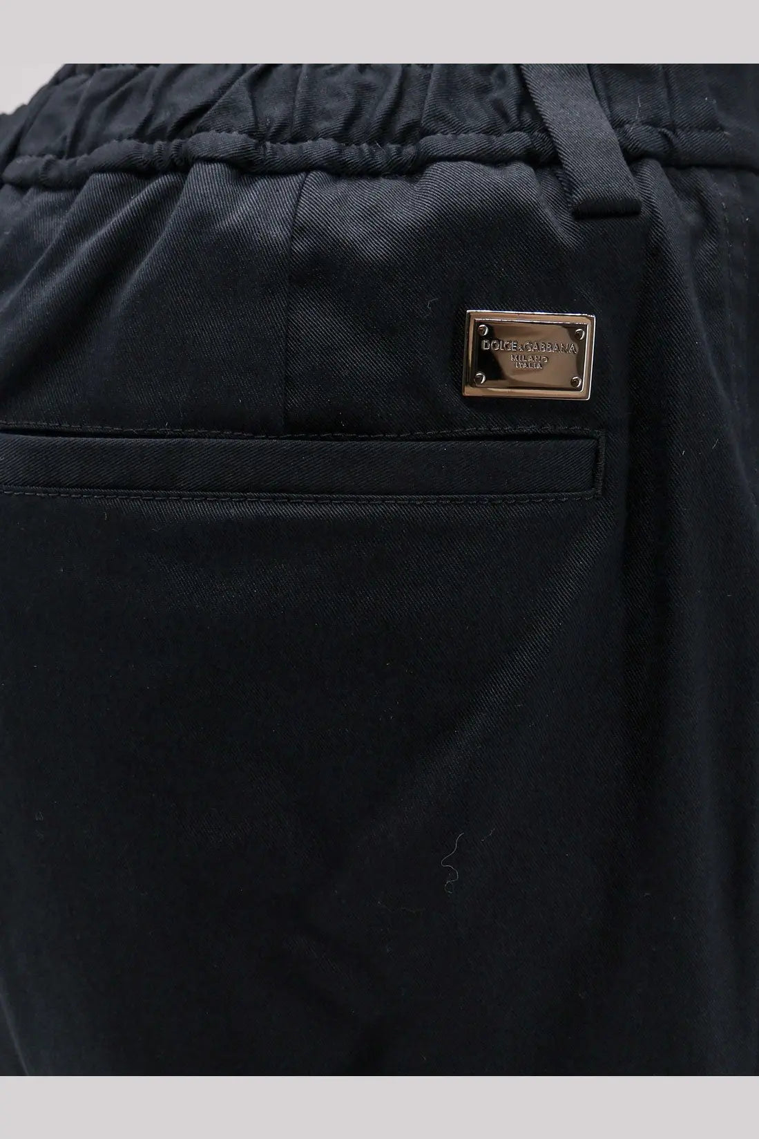 Back side of black cotton Dolce &amp; Gabbana men’s cargo trousers with metallic gold-tone brand plaque on the pocket