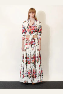 A woman wears a dolce and gabbana white cotton floral print two-piece outfit with a cropped shirt and tiered maxi skirt