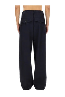 Black wide-leg cotton trousers with relaxed fit elastic waistband and buttoned front pockets for men by Dries Van Noten