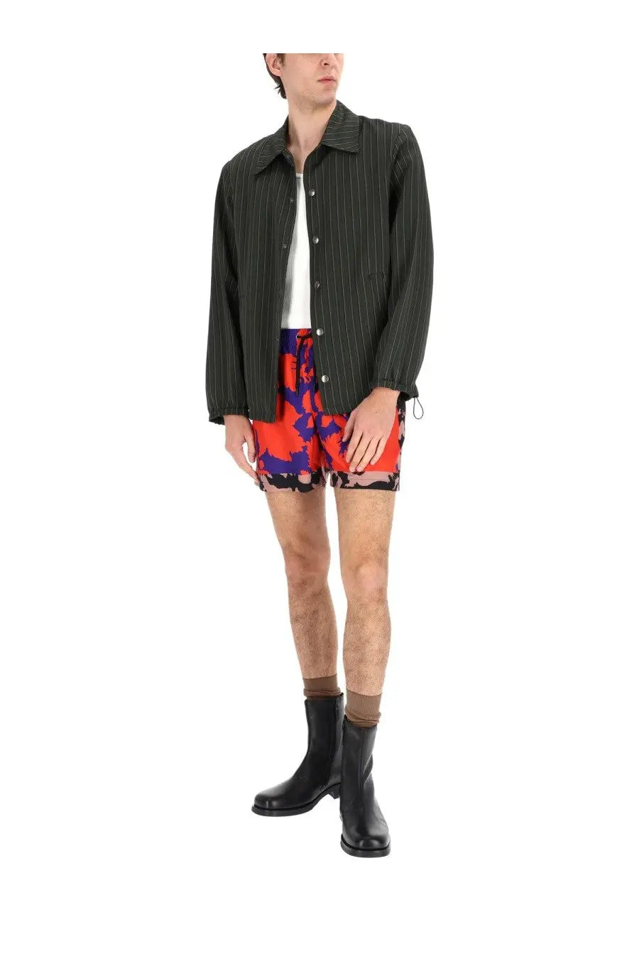 A man wearing a dries van noten men’s vorries jacket green over a white undershirt with colorful patterned shorts