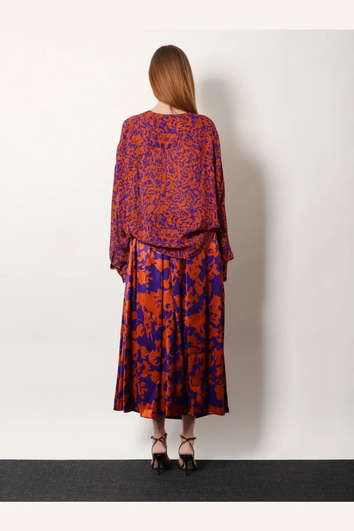 A woman wears a flowing two-piece cotton outfit in vibrant orange and deep purple floral print by Dries Van Noten