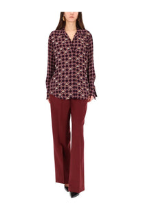 A woman wears a long-sleeved burgundy and cream geometric floral blouse paired with dries van noten women’s red pants