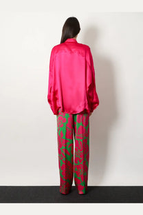A vibrant fuchsia satin blouse with relaxed fit and long sleeves paired with Dries Van Noten green viscose trousers