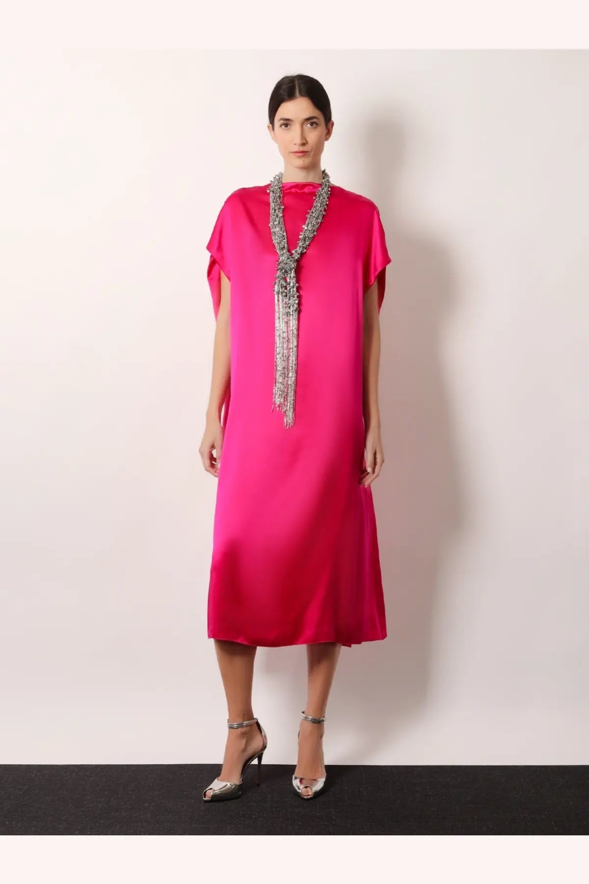 A vibrant fuchsia satin midi dress with short cape sleeves paired with a Dries Van Noten silver beaded scarf necklace
